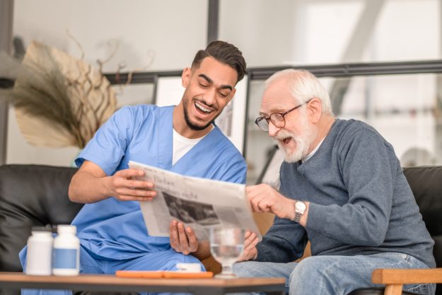 Old man and his caretaker laughing at a news item Independent Living Vs. Staying At Home: How To Decide
