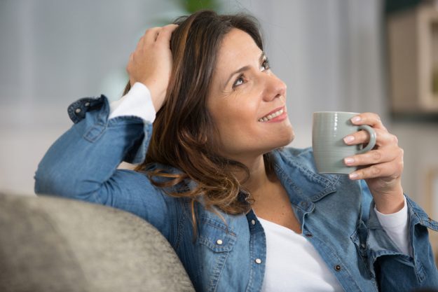 smiling woman sitting on sofa while drinking tea