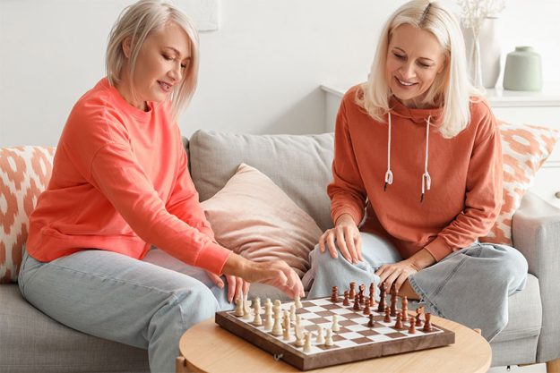 Mature female friends playing chess at home