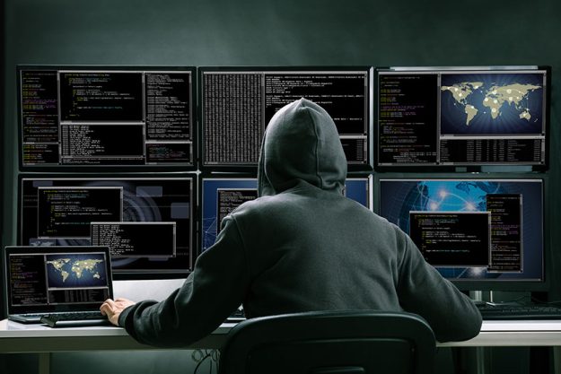 Rear View Of A Hacker Using Multiple Computer Rear View Of A Hacker Using Multiple Computer