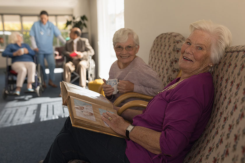 Side view of happy and smiling senior women with photo album looking at camera in home Side view of happy and smiling senior women with photo album looking at camera in home