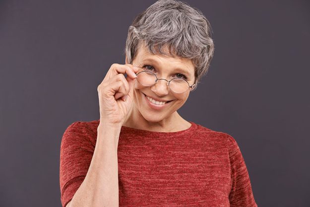 Happy, portrait and senior woman with glasses in studio for vision, optometry or frame sale on grey background. Eye care, testing or face of old lady model smile for pensioner, spectacles or discount.