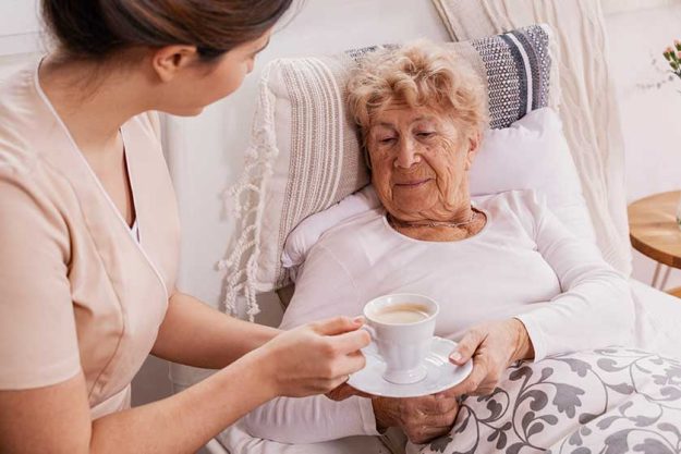 Beautiful young nurse serves tea to an elderly lady in a private nursing home Beautiful young nurse serves tea to an elderly lady in a private nursing home