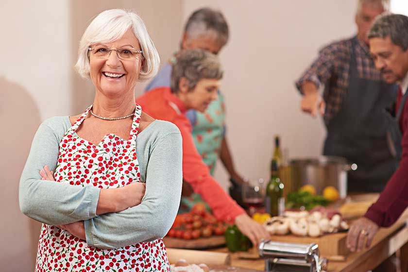 I love throwing dinner parties. Portrait of a senior woman with friends cooking together in the background. I love throwing dinner parties. Portrait of a senior woman with friends cooking together in the background.