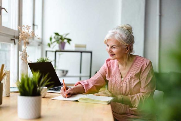Smiling mature businesswoman writing in notebook while sitting at table in office