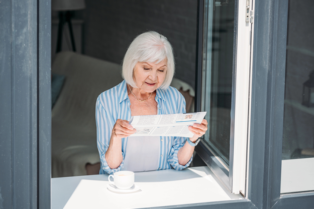 senior-woman-standing-windowsill Senior woman standing at windowsill with cup