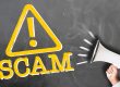 Hand holding megaphone against chalkboard with word SCAM