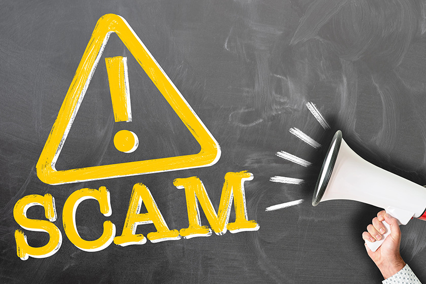 Hand holding megaphone against chalkboard with word SCAM